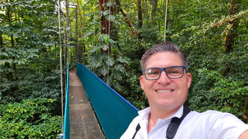 Yeudy Morera smiling beside a Heliconias hanging bridge surrounded by rainforest