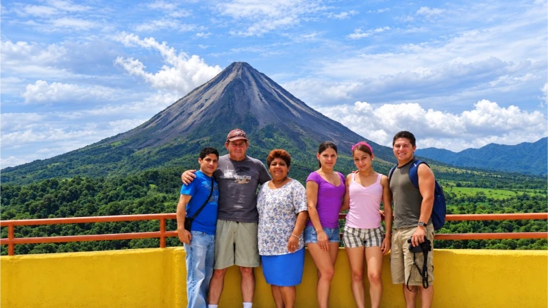 Six visitors at Místico Hanging Bridges with Arenal Volcano and forested slopes behind them.