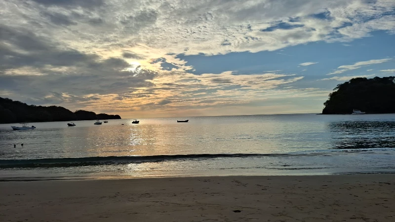 Small boats anchored off Playa El Jobo as late-afternoon light reflects across the bay between wooded headlands.